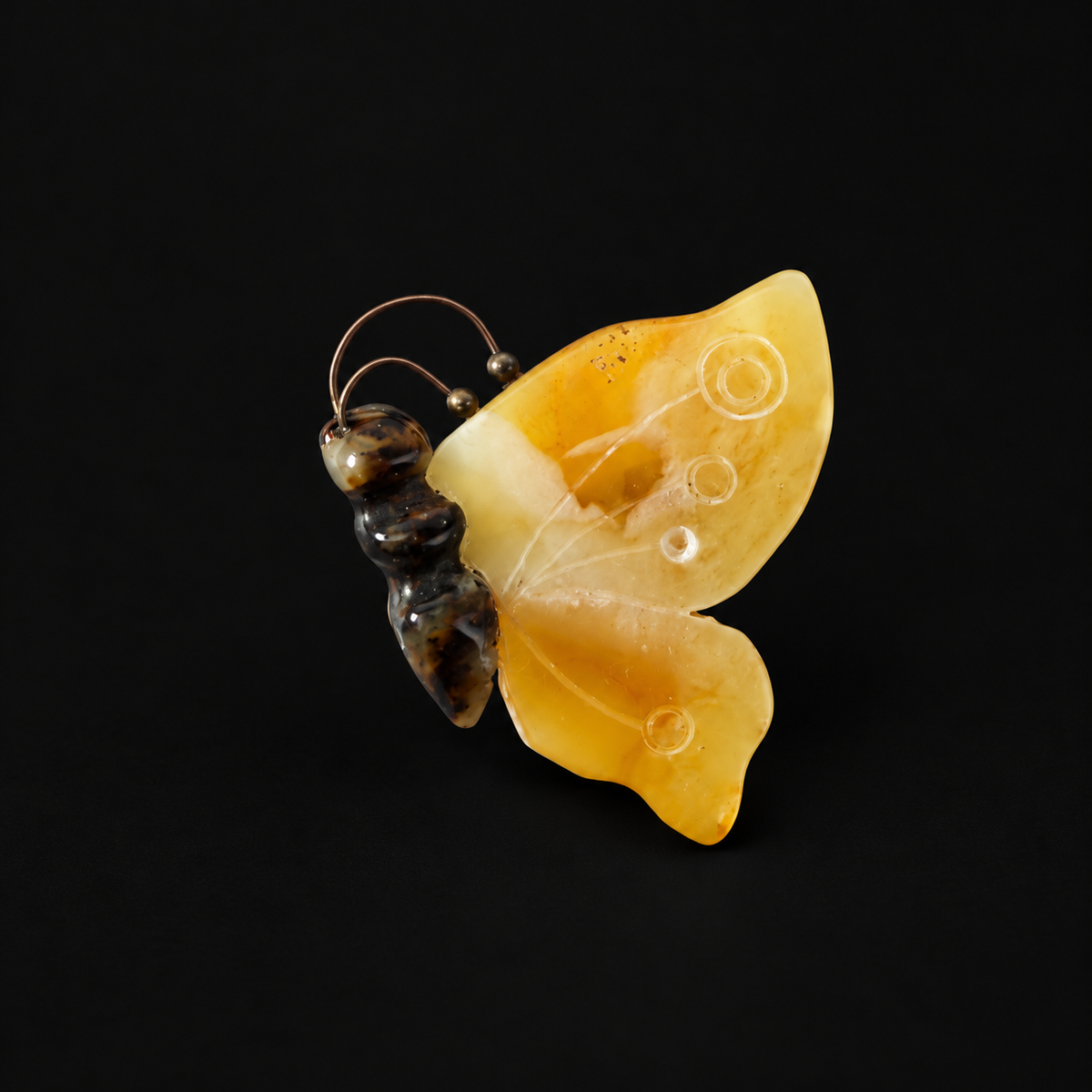 KIZIMA yellow amber butterfly brooch with carved circles and dark body on black background.
