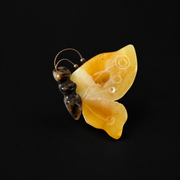 KIZIMA yellow amber butterfly brooch with carved circles and dark body on black background.