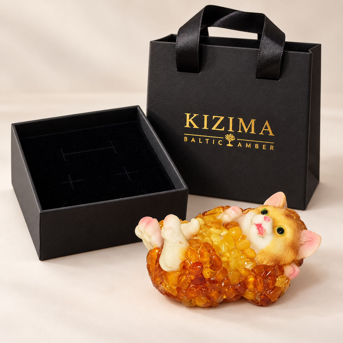 Baltic amber cat figurine on its back with black velvet-lined KIZIMA® gift box and gift bag — ready-to-give cat gift