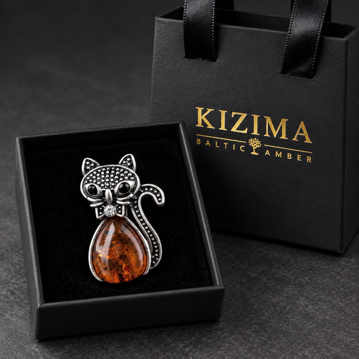 KIZIMA silver-tone cat brooch 20-205Q4-3-1-1 with cognac Baltic amber belly, black eyes and a crystal bow in the real black velvet KIZIMA gift box with matching bag.