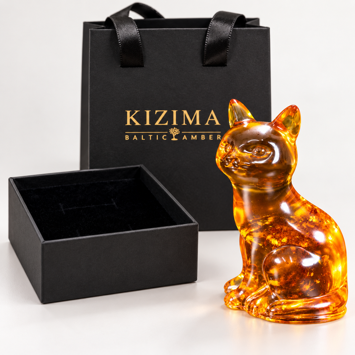KIZIMA cognac amber sitting cat beside a black velvet-lined gift box and branded gift bag