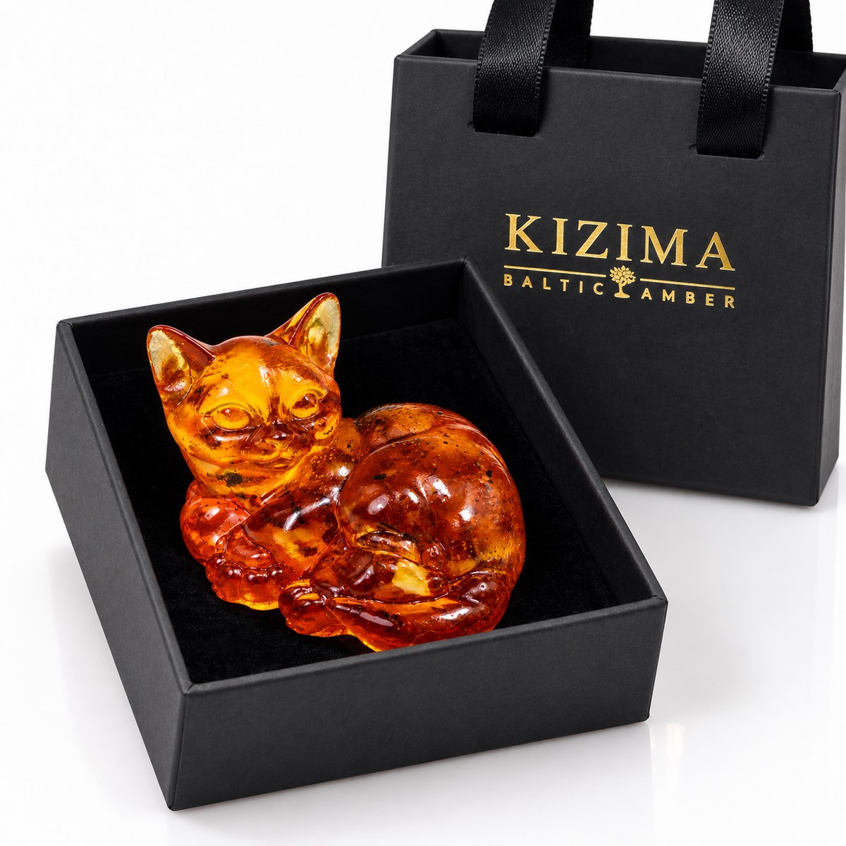 Curled amber cat inside an open black velvet-lined gift box with a KIZIMA bag