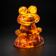 KIZIMA tiny frog figurine 9K0001q38 in translucent honey amber with natural dark inclusions, photographed on a premium black studio background.