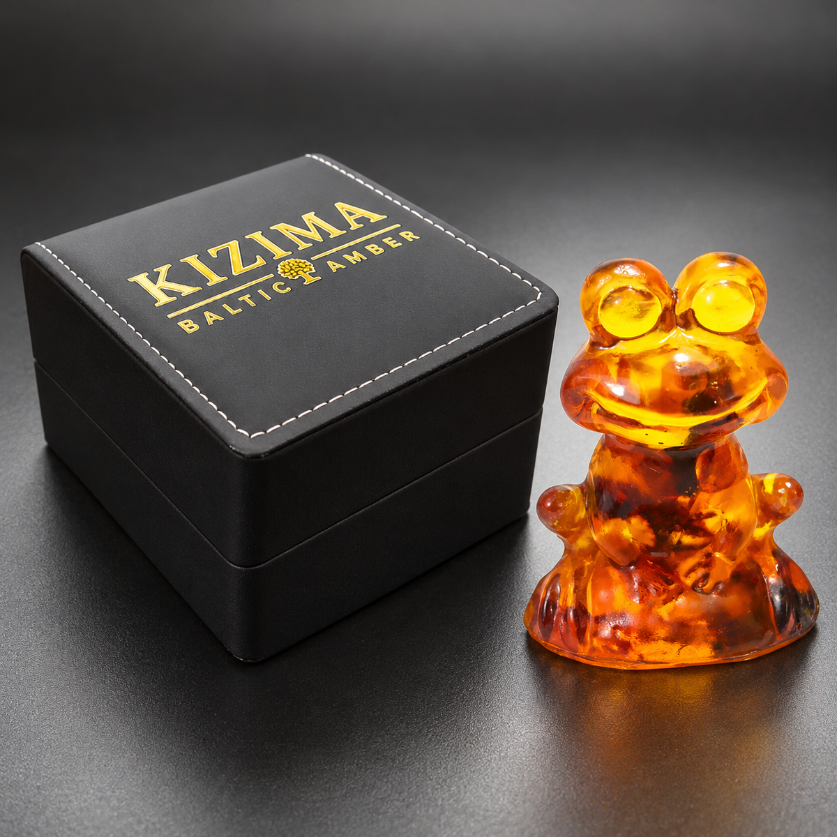 KIZIMA tiny amber frog figurine 9K0001q38 beside the genuine closed black stitched KIZIMA Baltic Amber gift box at proportional scale.