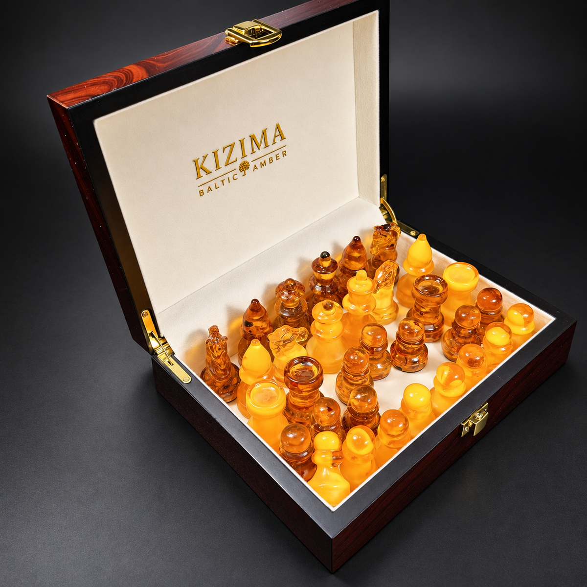 Golden yellow and cognac amber chess pieces inside an open KIZIMA presentation box with ivory lining, gold branding and a gold clasp.