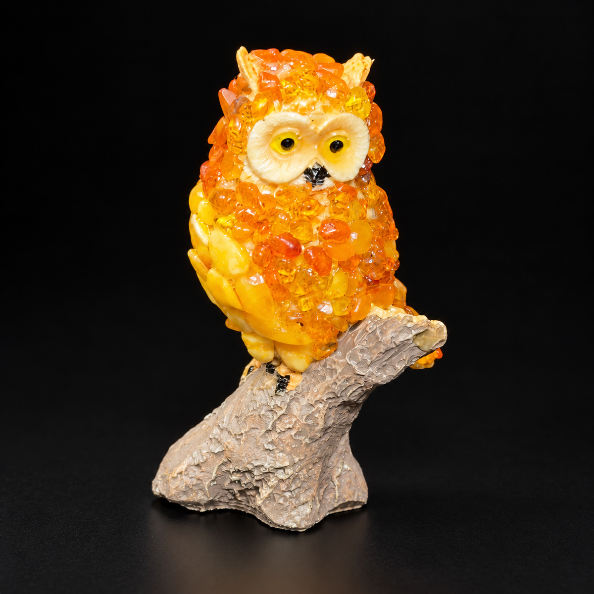 Golden-orange OWL24 owl figurine on its gray-beige branch stand against a black studio background
