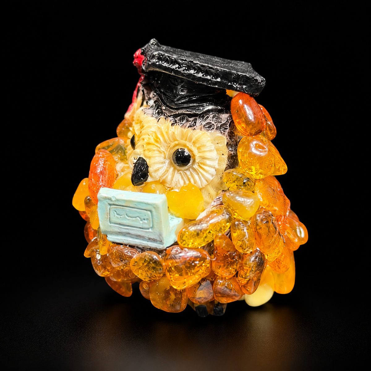 Golden orange graduation owl with black cap and pale turquoise detail on a black background