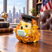 Made in USA natural Baltic amber graduation owl in a black cap on an oak desk with an American flag.