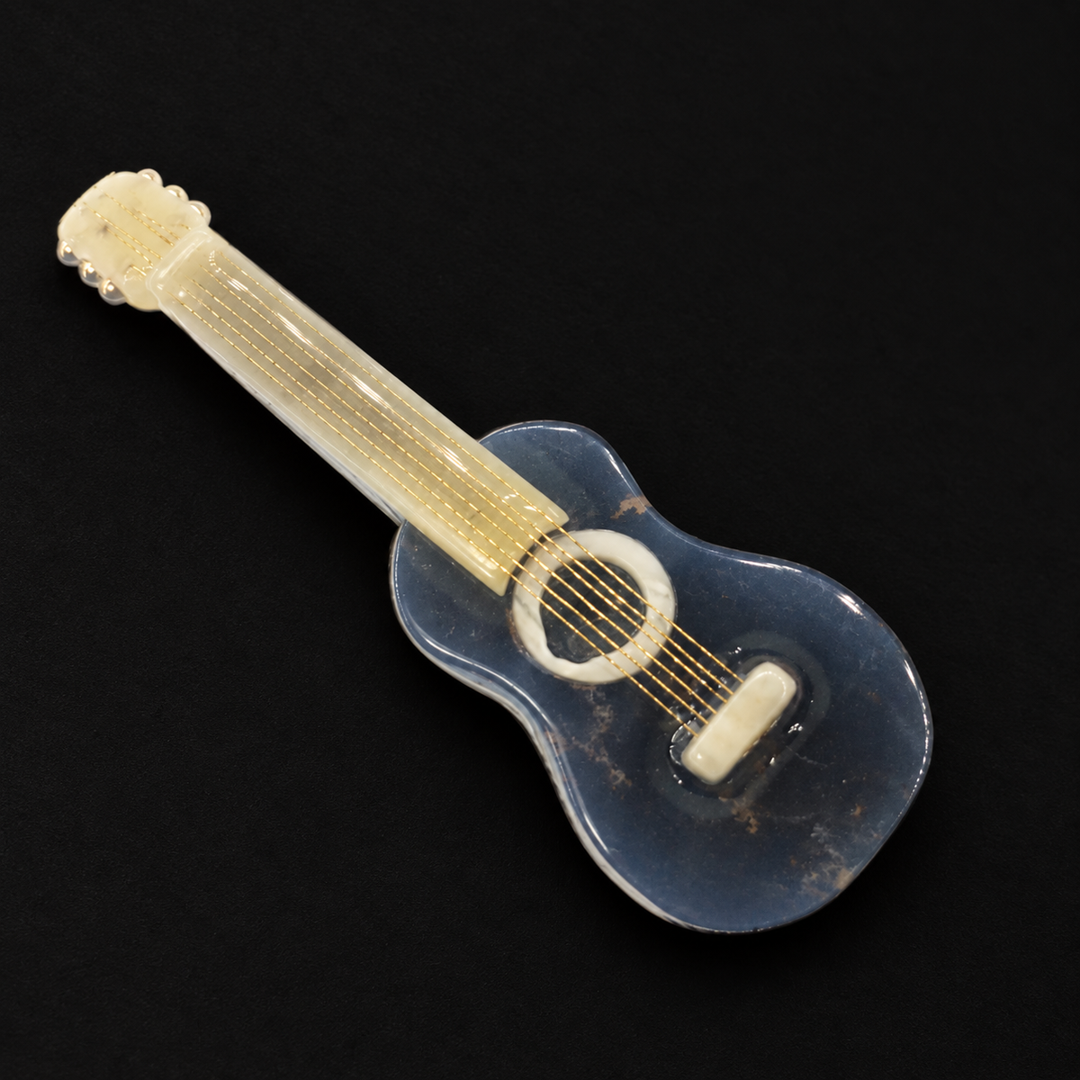 KIZIMA Baltic amber guitar brooch with blue-black body, cream neck and gold strings on a black studio background.