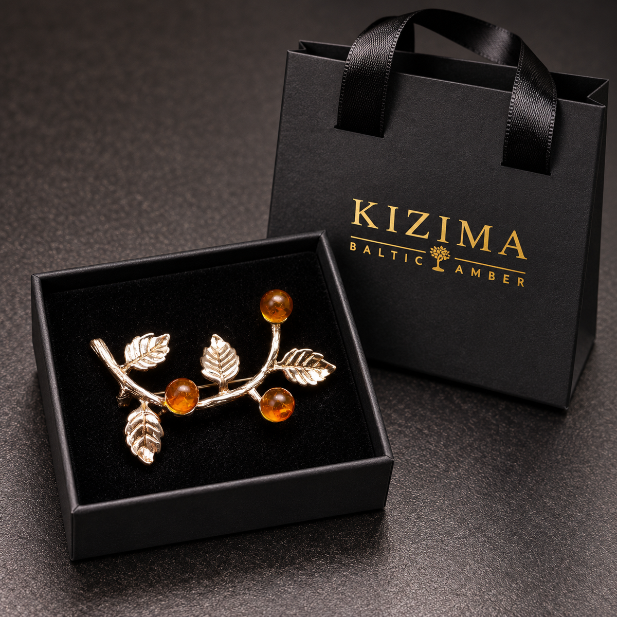KIZIMA curved leaf-and-berry brooch with three honey Baltic amber beads in the real black velvet gift box beside the gold-logo KIZIMA bag.