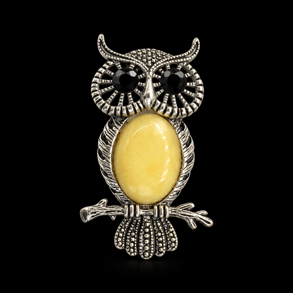KIZIMA silver-tone owl brooch with black eyes and opaque pale-yellow Baltic amber belly on black studio background.