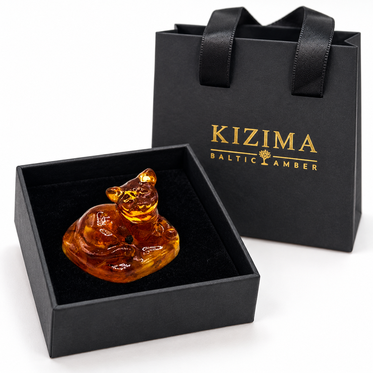 Reclining cat figurine in an open black velvet-lined box beside a gold-logo KIZIMA gift bag.