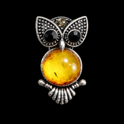 KIZIMA small silver-tone owl brooch with black eyes and honey-yellow Baltic amber belly on black studio background.
