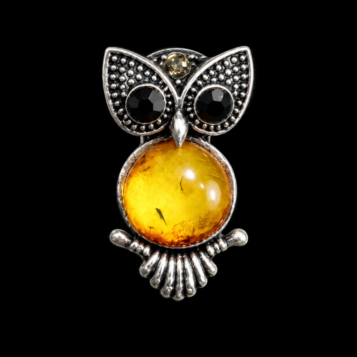 KIZIMA small silver-tone owl brooch with black eyes and honey-yellow Baltic amber belly on black studio background.