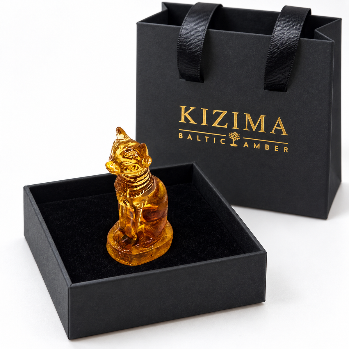 Sphinx cat figurine in a black velvet-lined gift box beside the gold-logo KIZIMA bag.