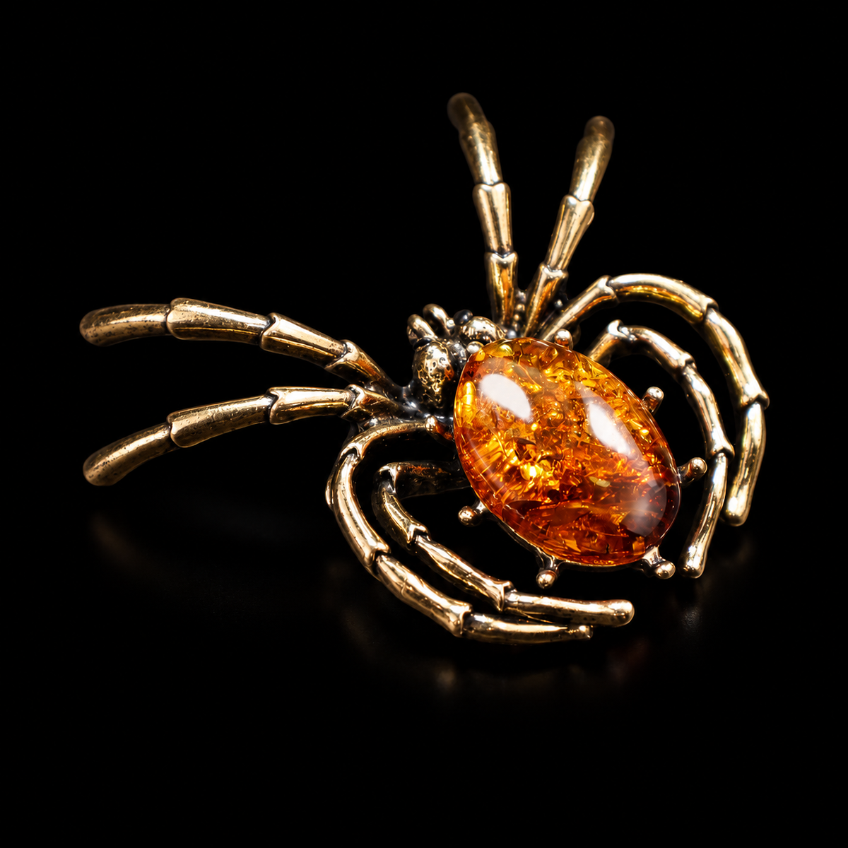 KIZIMA antique-gold-tone spider brooch with oval cognac Baltic amber on black studio background.