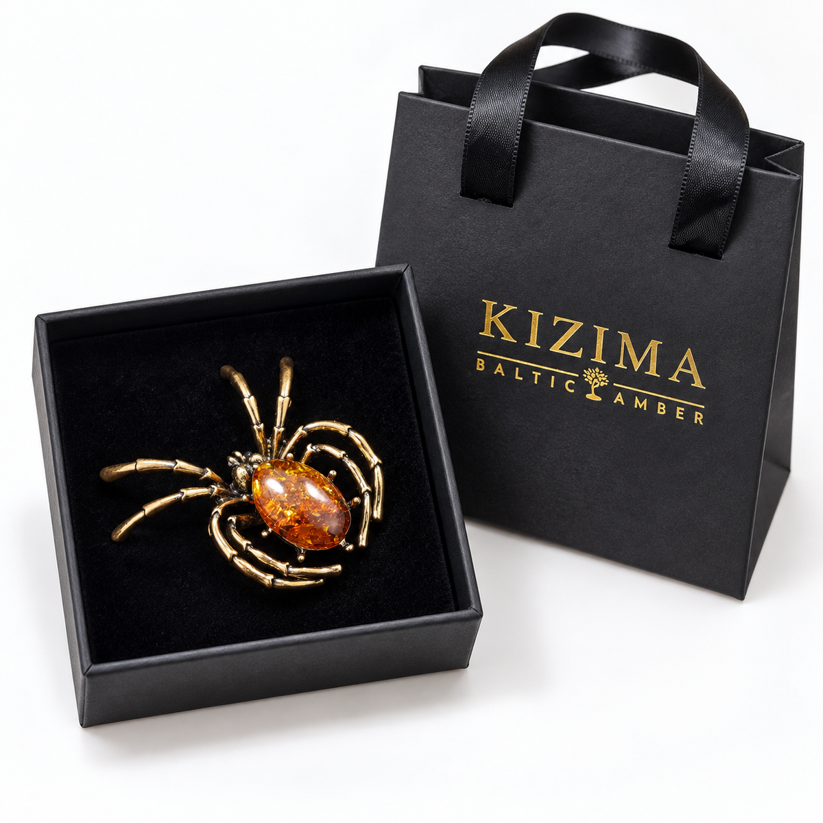 KIZIMA antique-gold-tone spider brooch with oval cognac Baltic amber in actual black KIZIMA gift packaging.