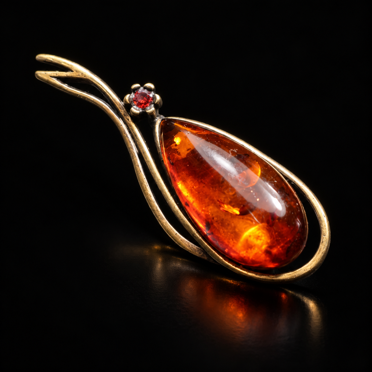 KIZIMA antique bronze-tone teardrop brooch with reddish cognac Baltic amber and a small red accent stone on a black studio background.
