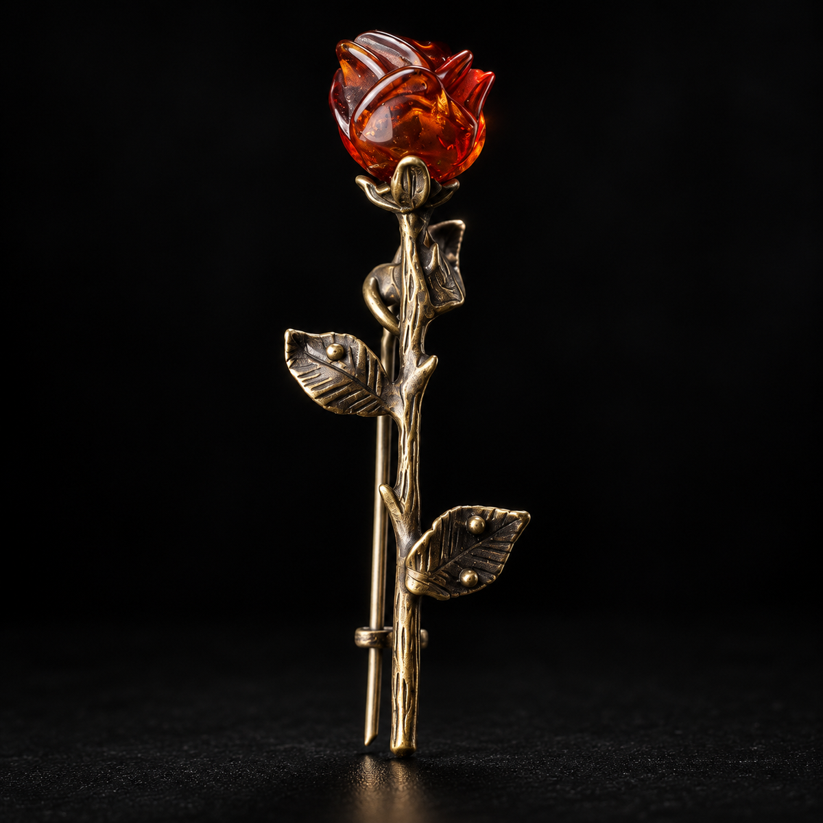 KIZIMA antique bronze-tone rose brooch with a reddish cognac amber bud and three veined leaves on a black studio background.