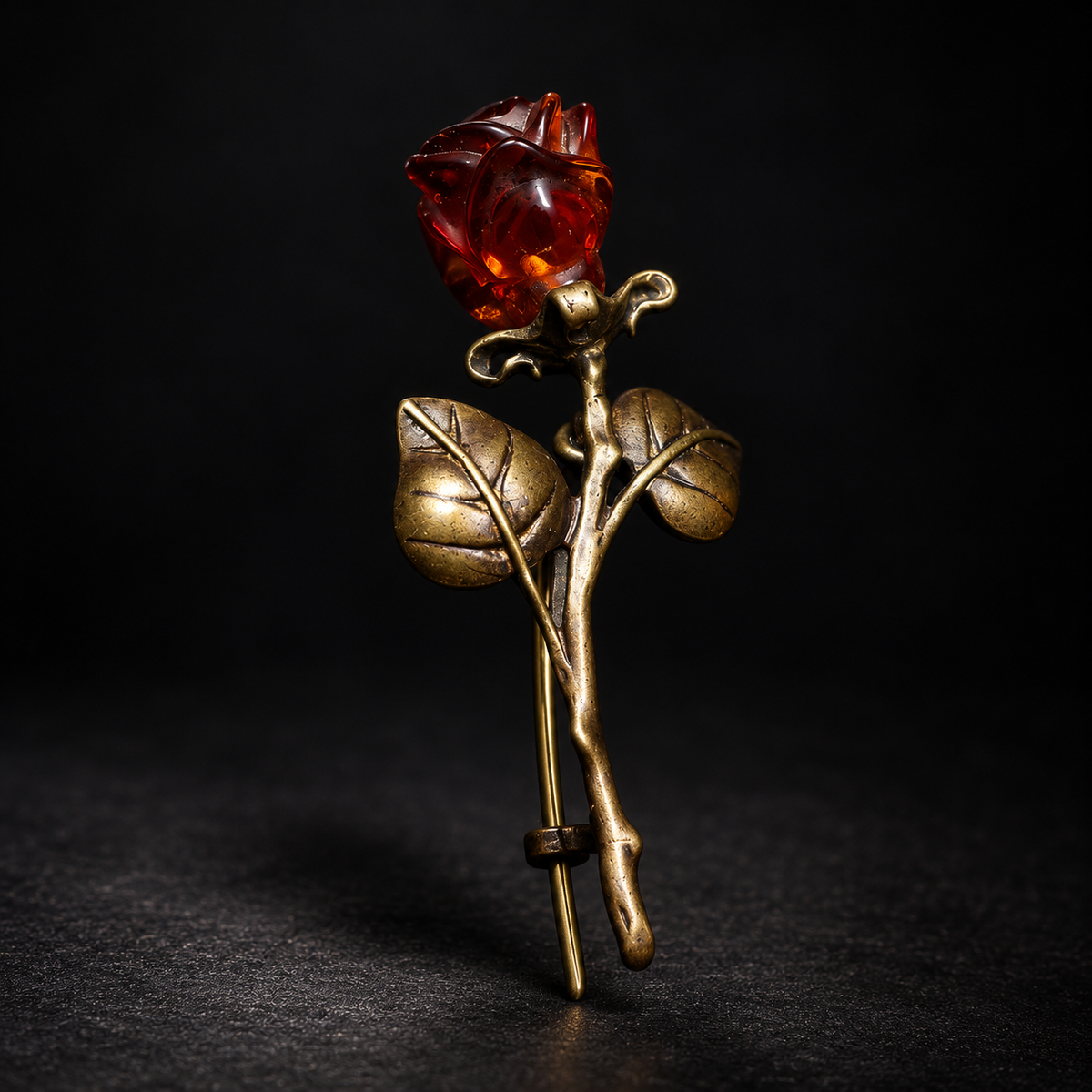 KIZIMA antique bronze-tone rose brooch with a deep cognac amber bud and two rounded leaves on a black studio background.