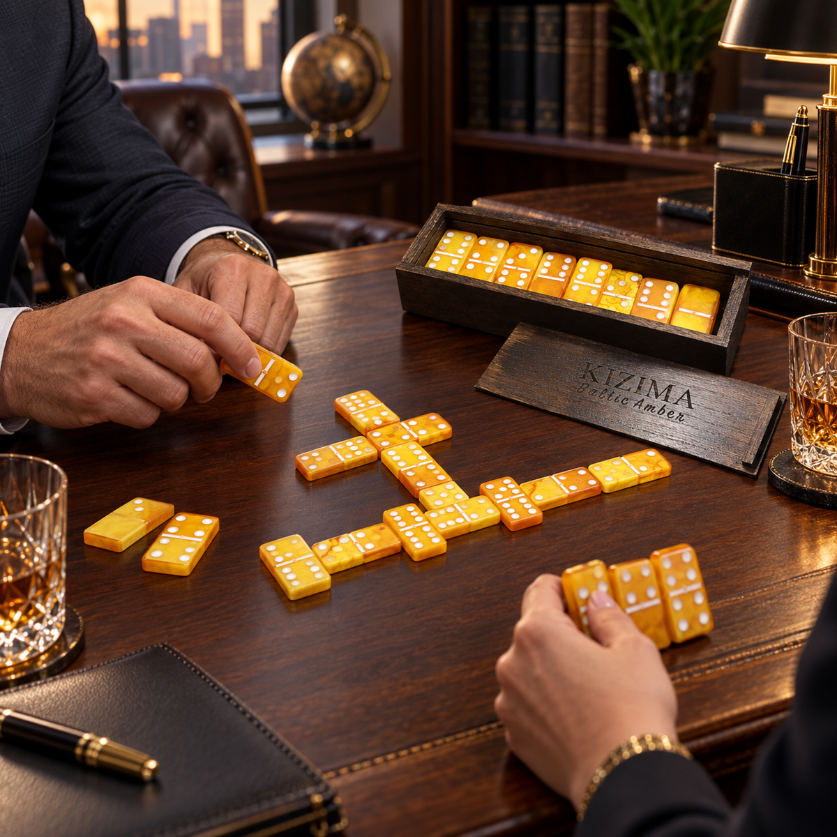 Two people playing dominoes with honey-colored Baltic amber tiles on executive desk, KIZIMA® wooden case — unique game gift for men, Made in USA