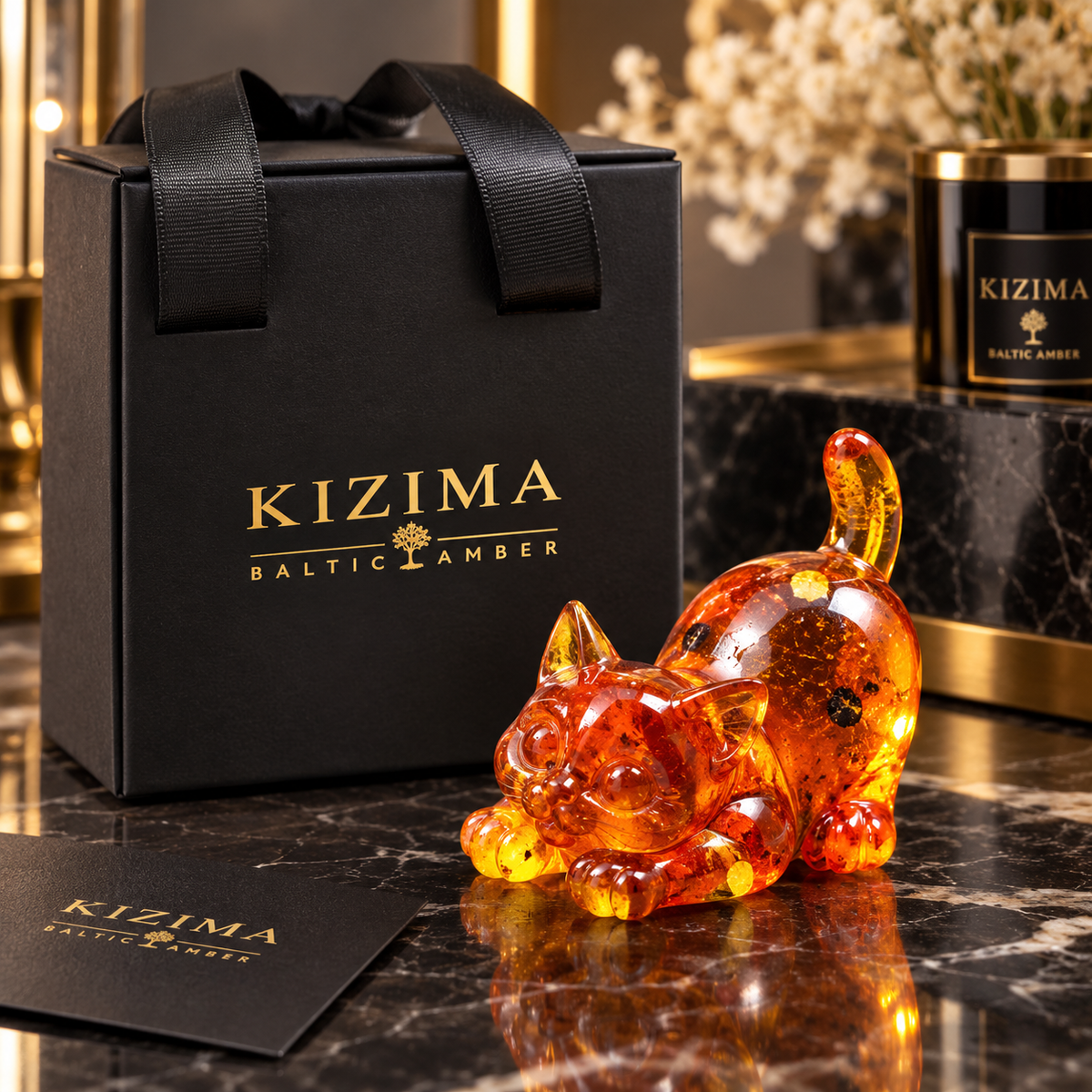 Made in USA natural Baltic amber golden cat figurine by KIZIMA® with black KIZIMA gift bag and box on a marble desk — playful stretching cat, cat lover gift
