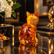Made in USA natural Baltic amber sitting cat figurine by KIZIMA® on a marble desk with white flowers — cognac amber with golden inclusions, cat lover gift