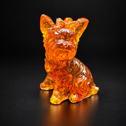Amber Yorkshire Terrier figurine on black, with pointed ears, a bow between them and a carved beard above its forward paw.