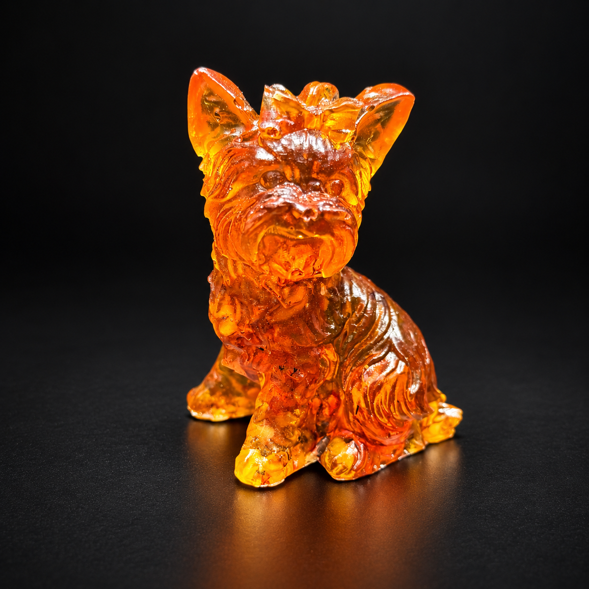 Amber Yorkshire Terrier figurine on black, with pointed ears, a bow between them and a carved beard above its forward paw.