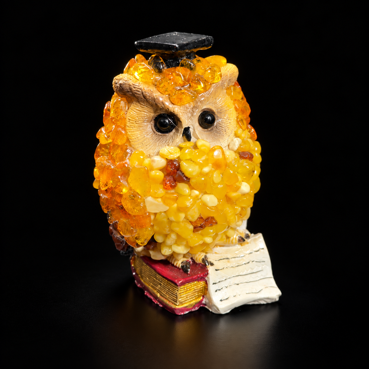 Golden yellow scholar owl figurine with black graduation cap on a black studio background